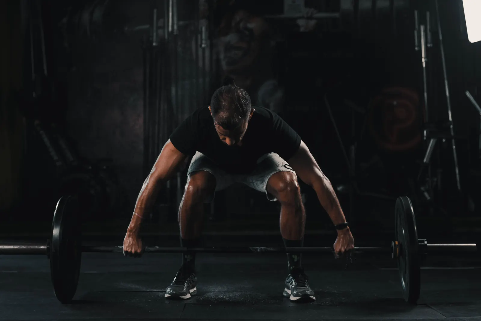 Athlete preparing for a barbell deadlift in a dark home gym